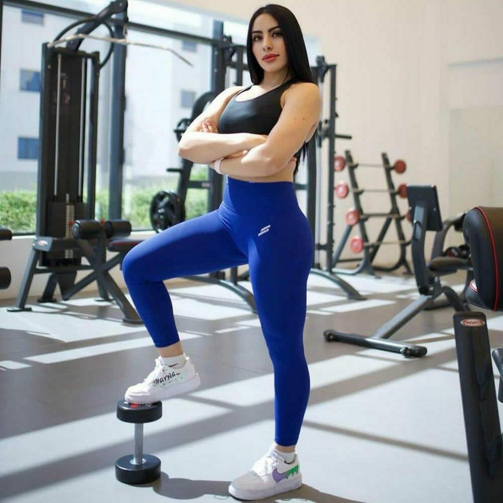 A woman in blue leggings posing in a gym.