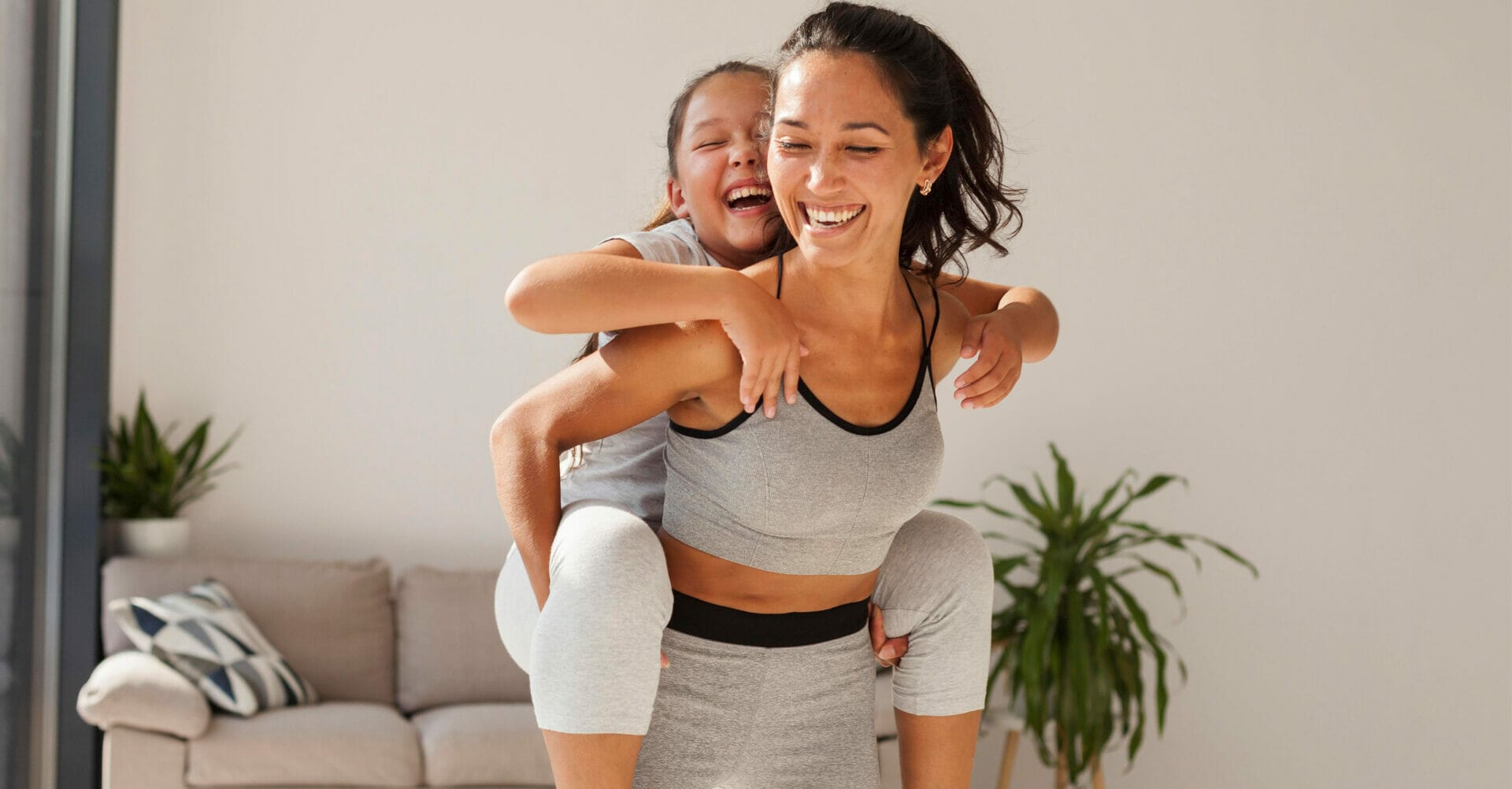 Busy mom and daughter engage in piggyback exercise at home.