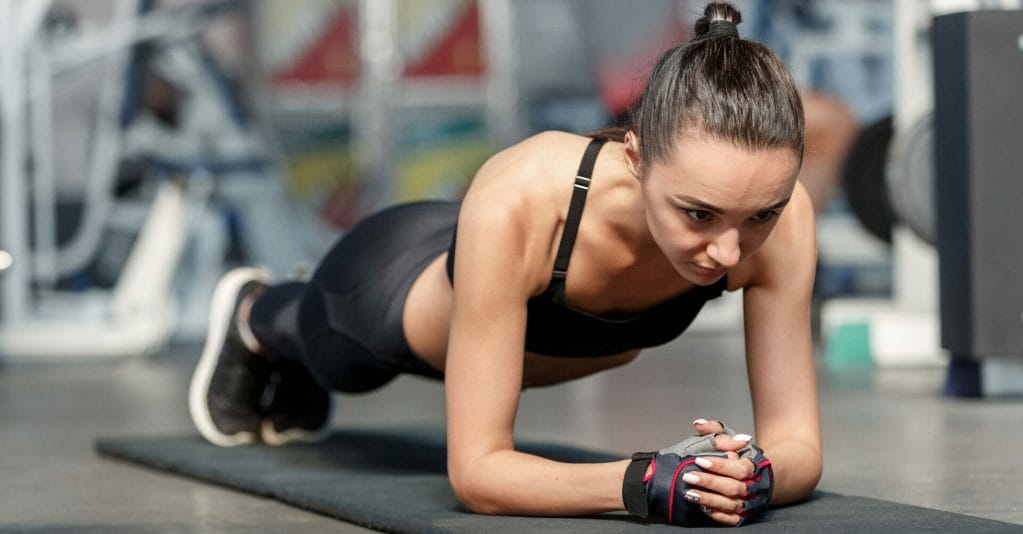 A woman is strengthening her core by doing push ups at the gym.